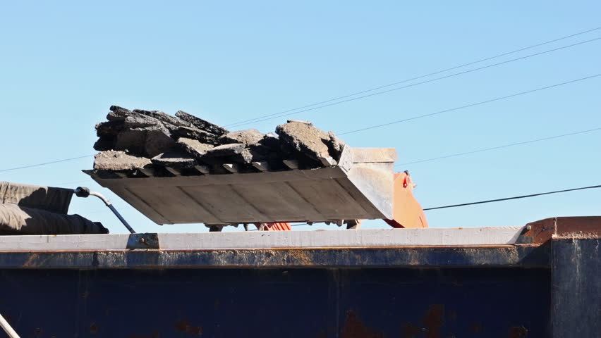 Workers use large machinery to break concrete, asphalt in construction site under road works