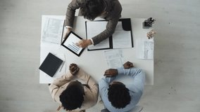 Top view of African American couple sitting across desk from male financial advisor reviewing graphs on tablet during daytime business meeting in office. - Powered by Shutterstock - Get 15% off with code: PIKWIZARD15
