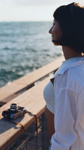 Vertical shot. Close-up from the side: a stylish woman taking a photo with a film camera on the beach. Girl photographer.