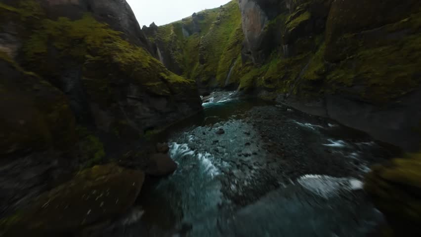 Dynamic low-altitude flight following the path of a river through ancient mossy rock walls.