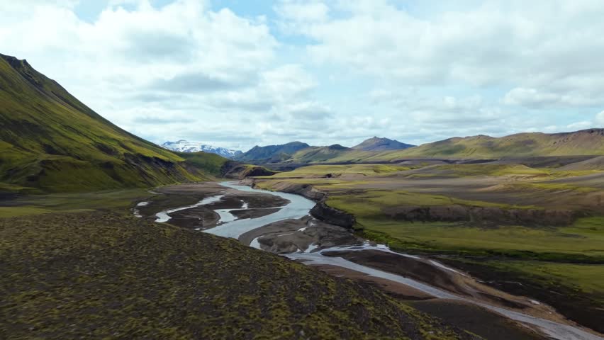 Wide angle drone shot of a blue river carving through a vast green and brown mountain landscape.