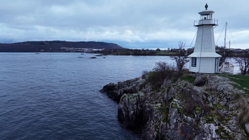 A peaceful coastal landscape featuring a small white wooden lighthouse on a rocky peninsula by the sea.