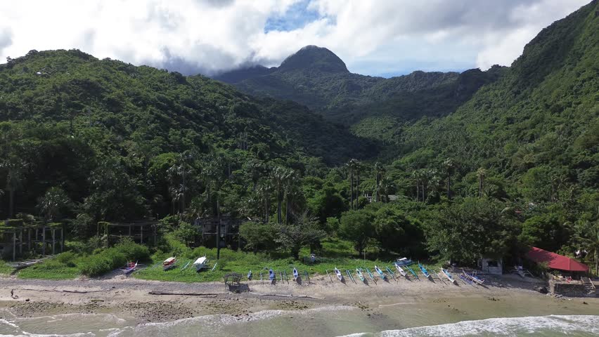 Aerial drone footage of boats resting at Aninuan Beach in Puerto Galera Philippines with crystal clear water sandy beach dense forest and green mountains in the background forming a tropical landscape