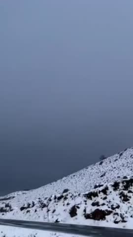 Snow-covered mountain slope under a cloudy gray sky. Minimal winter landscape with rocky terrain and fresh snowfall, creating a cold, moody, and atmospheric natural scene suitable for nature, travel, 