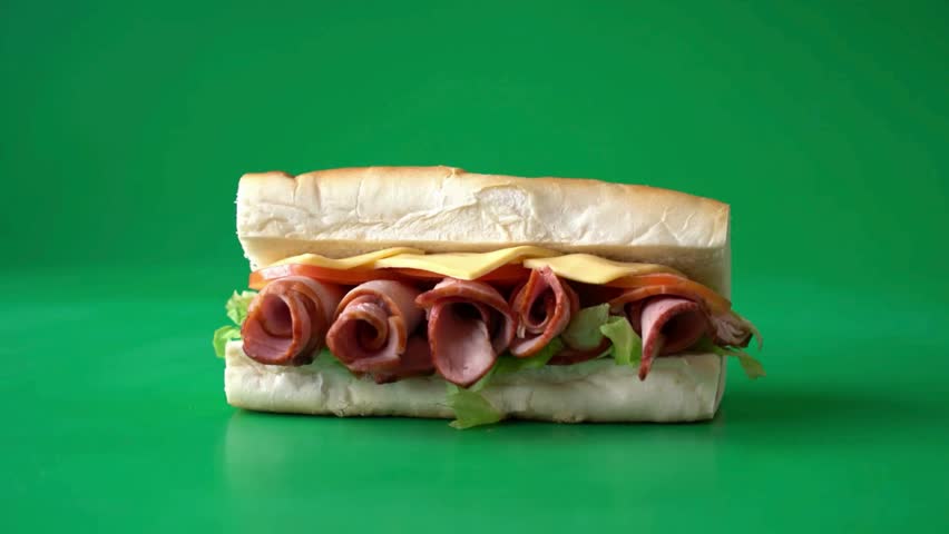 A professionally lit studio shot featuring a delicious submarine sandwich with layers of rolled deli ham, sliced cheese, crisp lettuce, and fresh tomatoes on a soft white sub roll. The sandwich rotates a full 360 degrees against a vibrant green screen background, making it an ideal asset for food commercials, restaurant menus, and digital marketing content requiring easy background replacement.