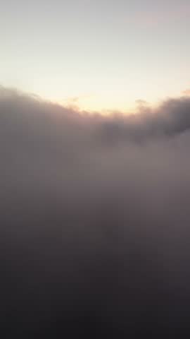 Aerial view flying through a thick layer of rolling clouds during a beautiful golden hour sunset
