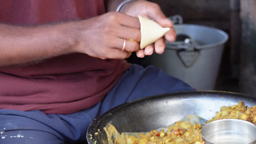 A person is preparing a samosa by filling stuffing inside the puri