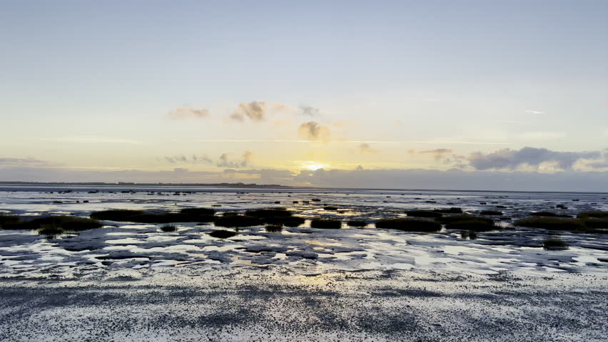 Low tide sunset on Le Crotoy beach in Somme Bay, France, with reflective tidal flats, sandbanks and dramatic clouds over a calm coastal seascape, golden horizon