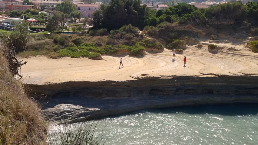 Scenic view of tourists walking on the unique sandstone rock formations of Canal d'Amour in Sidari Corfu Greece overlooking the turquoise Ionian Sea on a sunny summer day