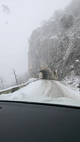Morning snowstorm on a mountain road in Montenegro with low visibility and rocky landscape.