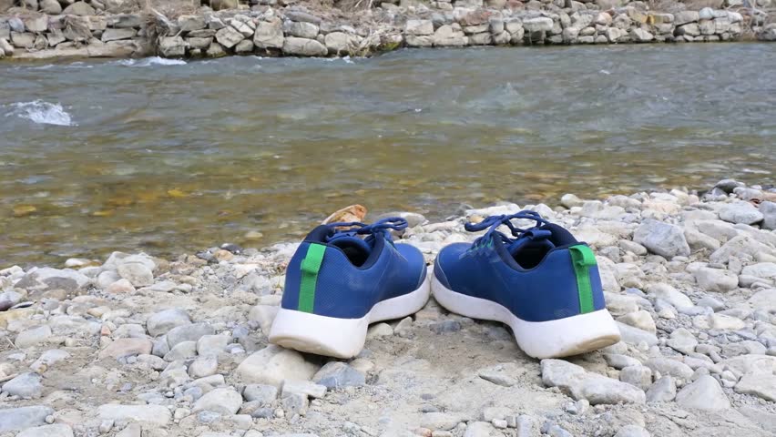Pair of sports shoes resting on riverbank.