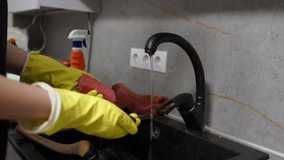 Cleaning dishes with sponge at kitchen sink while wearing yellow gloves and water running in evening - Powered by Shutterstock - Get 15% off with code: PIKWIZARD15