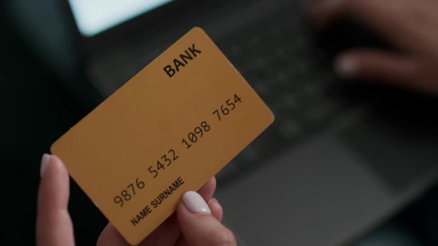 Close-up of a manicured female hand with white nails holding a credit card and typing on a laptop, ideal for online shopping, e-commerce, and finance.