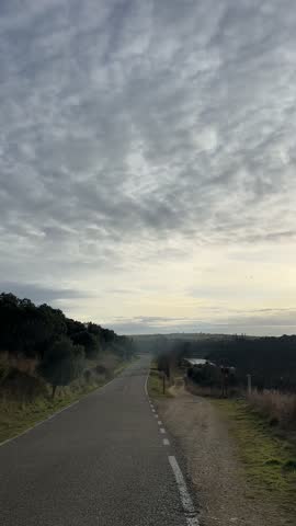 Sweeping shot along a country road unveils a stunning mountain lake vista in the midst of a cloudy sunset. Serene and tranquil surroundings
