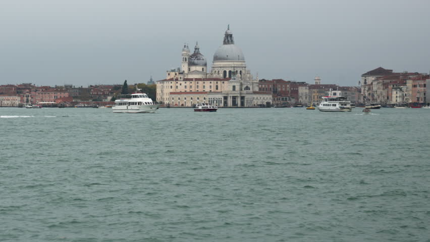 Santa Maria della Salute Basilica and boats in the Venetian lagoon under cloudy sky. Public water transport and historic architecture in Venice, Italy, on an overcast and gloomy day.