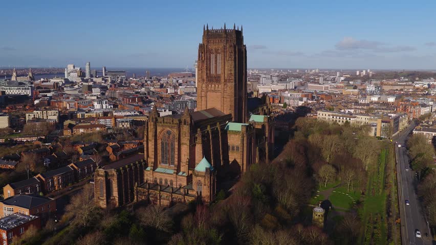Aerial sunrise pullback over Liverpool, UK, shows Liverpool Cathedral, Pier Head, Albert Dock, River Mersey, port cranes, wind turbines, ferris wheel, and brick terraces.