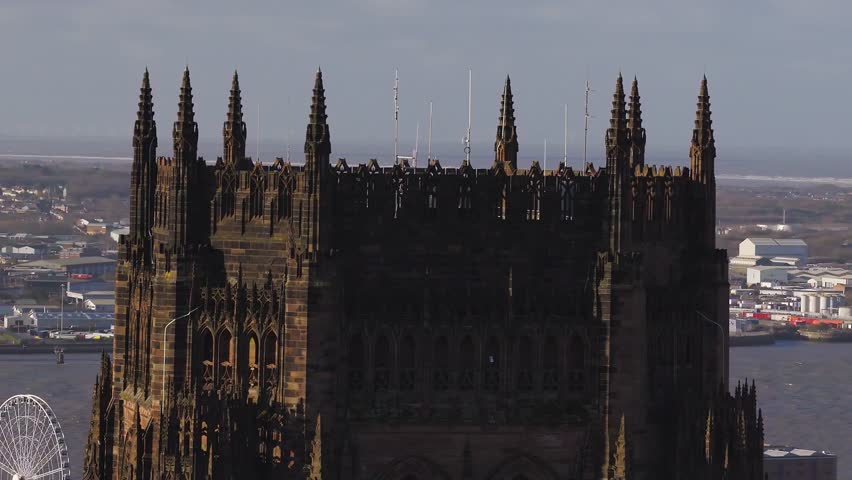 Aerial drone pans and pulls back from Liverpool Cathedral at sunrise. The River Mersey, Ferris wheel, and Tate and Liverpool Museum area appear in warm sidelighting.