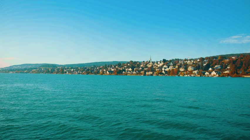 Lakeside settlement near Zurich featuring residential buildings along the shoreline with green hills.