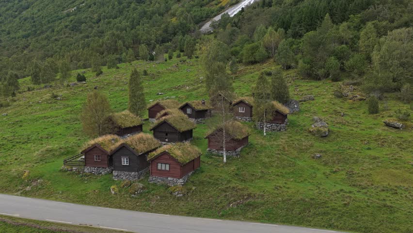 Aerial view of cabins by clear lake and rugged peaks, Norway. Aerial drone video