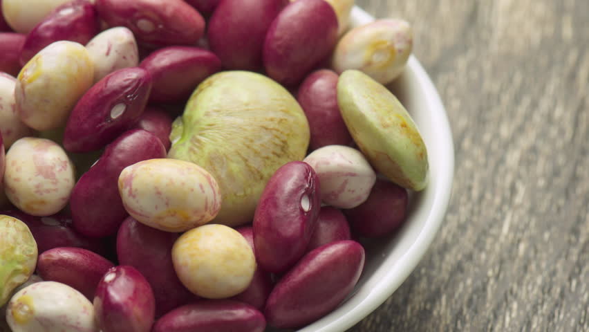 Fresh beans of different varieties and sizes on white plate. Macro shot. Colorful beans on wooden table. Product of organic farming. Healthy eco vegetarian food.