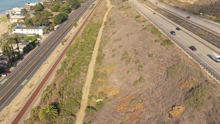 Aerial view of a California coastal town with seaside houses, highway, and mountains along the Pacific Ocean.