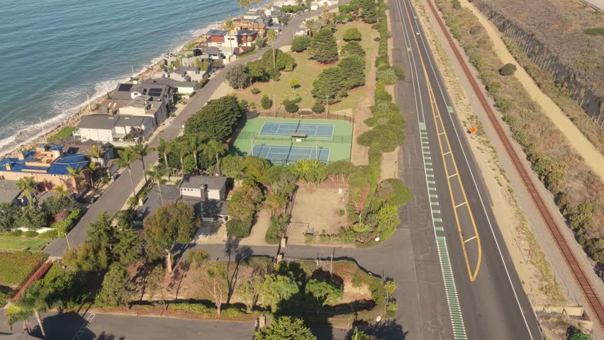 Aerial view of a California coastal town with seaside houses, highway, and mountains along the Pacific Ocean.