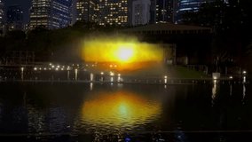 A cutting-edge water and light show transforms a city park lake into a stage for modern celebration. This horizontal footage captures a large-scale installation projecting a vibrant digital sunset over hills, enhanced by dynamic water effects and colorful lighting. The spectacular glow reflects on the rippling water, with illuminated skyscrapers creating a stunning urban nightscape backdrop. Perfect for advertising innovative event technology, promoting urban festivals, concert visuals, or as dynamic b-roll for projects related to entertainment, tourism, and futuristic city life. - Powered by Shutterstock - Get 15% off with code: PIKWIZARD15