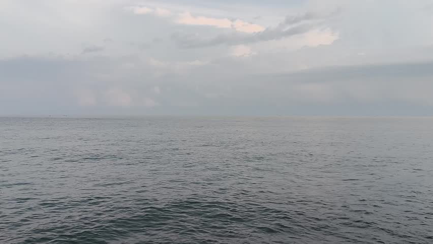 Calm sea waves under a cloudy sky with coastal hills in the distance. 
