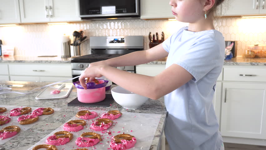 With focused attention, this budding culinary artist dips pretzels into a pot of melted chocolate, creating sweet delights in the warmth of a well-lit home kitchen.