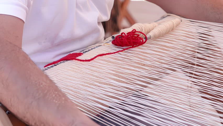 Red yarn is threaded through white warp threads on a wooden handloom as part of the weaving process.