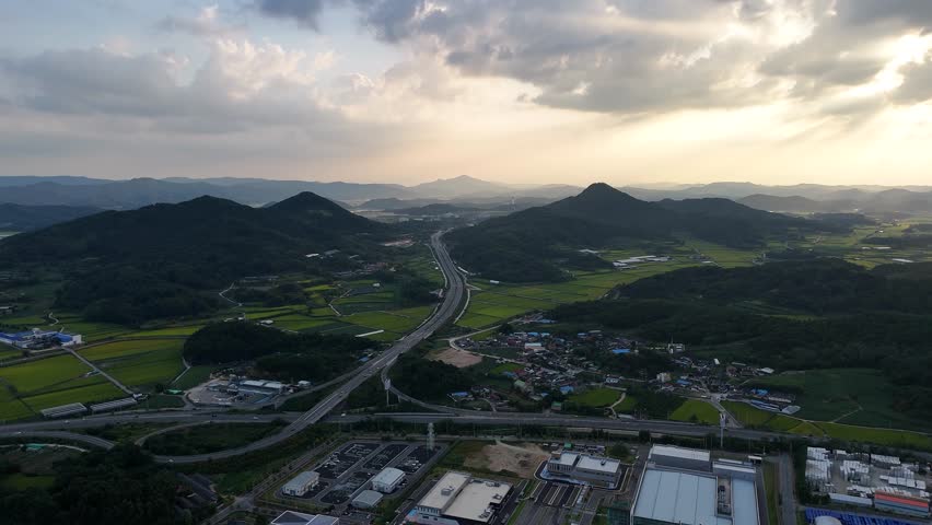 Aerial view of beautiful green rice fields and rural villages nestled in a valley surrounded by mountains during Summer Sunset in South of Korean