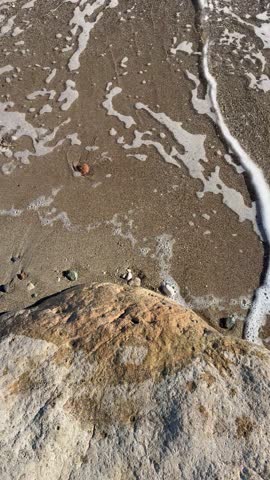 Close-up of small sea waves washing over coastal rocks near the shore. Natural texture of wet stones and moving water, shoreline detail, soft motion, coastal surface