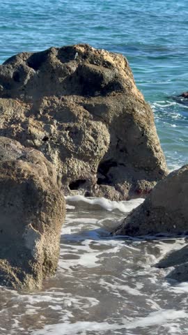 Close-up of small sea waves washing over coastal rocks near the shore. Natural texture of wet stones and moving water, shoreline detail, soft motion, coastal surface