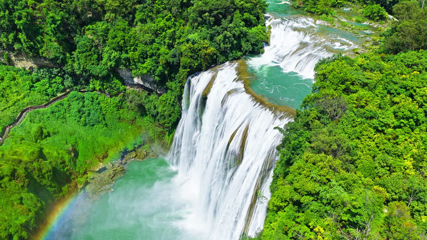The famous Huangguoshu Waterfall natural landscape in Guizhou, China. Aerial shot of a magnificent large waterfall cascading down into a turquoise pool surrounded by lush green tropical forest in summer.