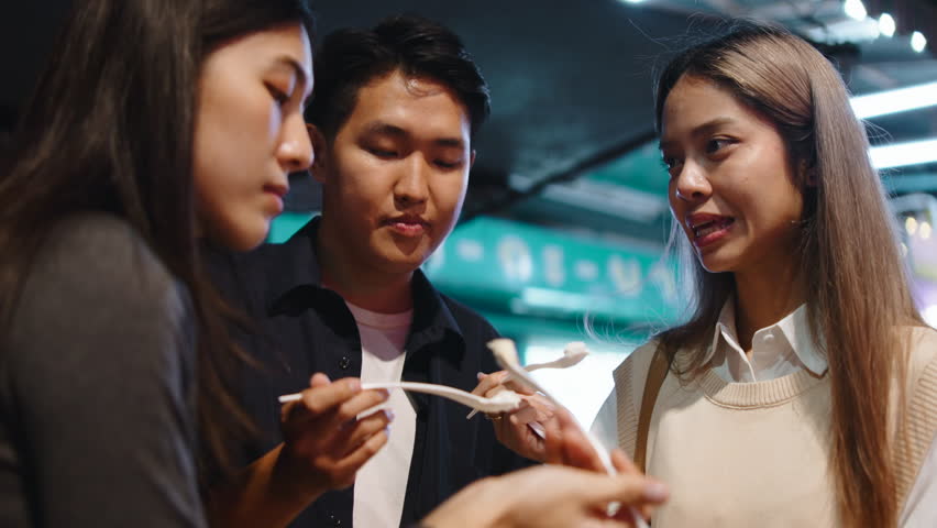 Young asian friends eating street food at night market