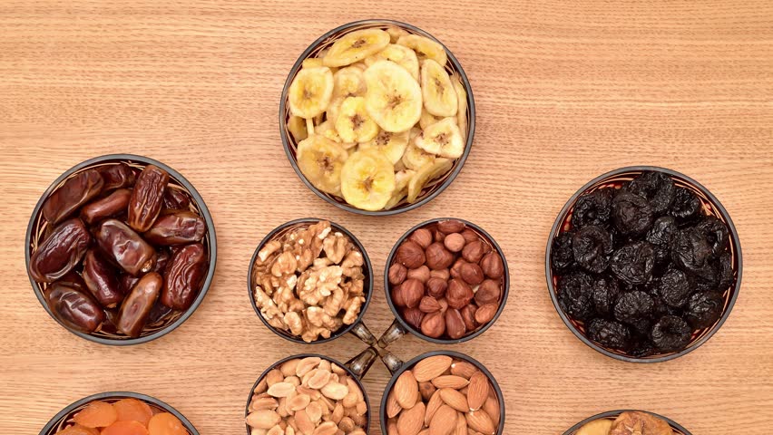 Dried fruits and different types of nuts in decorative glass bowls on the wooden table. Top view. Tilt down shot. Healthy eating concept.