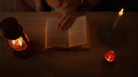 Top down view of woman hands turning pages of book on wooden table, illuminated only by warm glow of kerosene lamp and candles during complete blackout at night - Powered by Shutterstock - Get 15% off with code: PIKWIZARD15