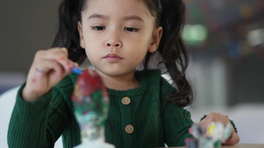 child girl painting plaster statue on the table