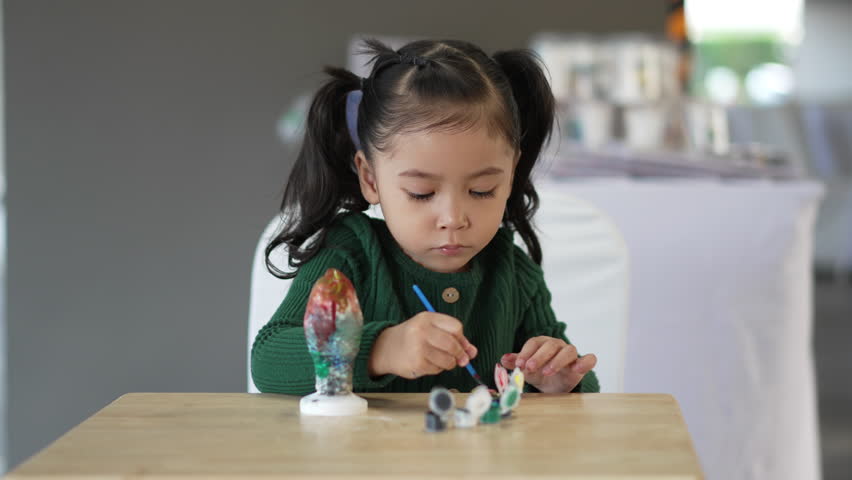 slow motion of child girl painting plaster statue on the table