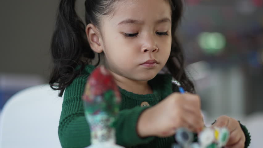slow motion of child girl painting plaster statue on the table