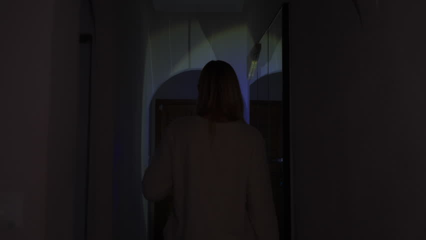 Worried woman using flashlight to navigate her dark home during sudden blackout, checking  fuse box in corridor as she deals with electricity shortage and energy crisis