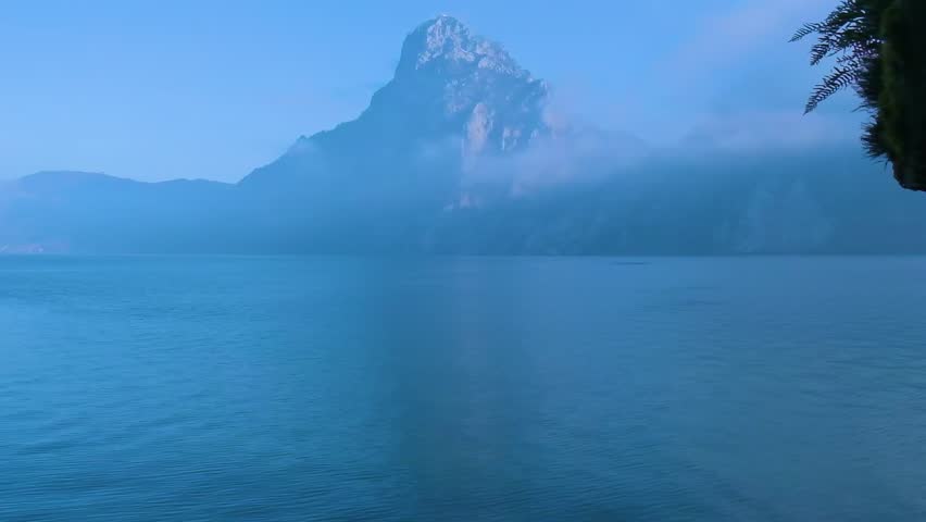 Static shot of calm alpine lake with mountain in background under clear sky. Peaceful nature landscape and travel concept.