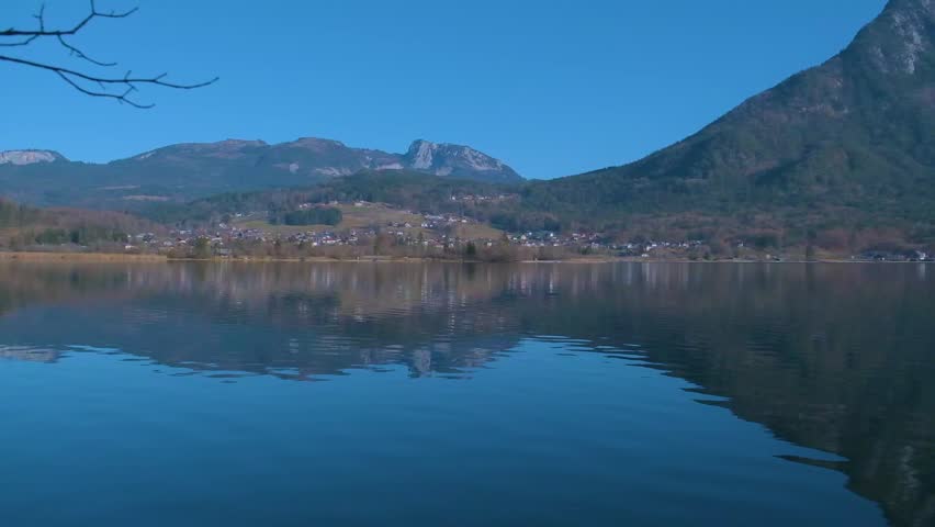 Static shot of calm alpine lake with mountain in background under clear sky. Peaceful nature landscape and travel concept.