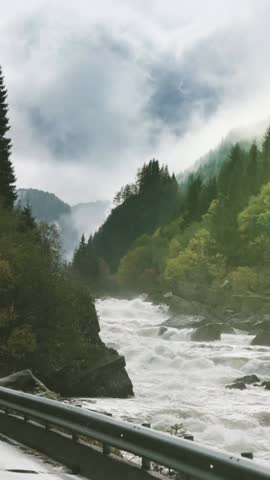 Dynamic white water rapids footage in norwegian mountain landscape with misty forest and dramatic cloudy sky