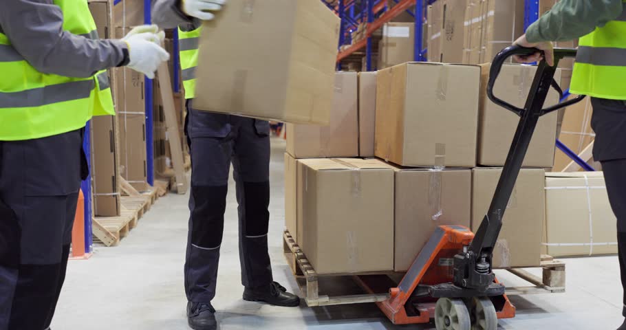 Warehouse workers loading pallet boxes for shipping. Manual pallet jack moves cartons in a distribution warehouse for efficient transport and safe loading. Strong concept of delivery logistics.