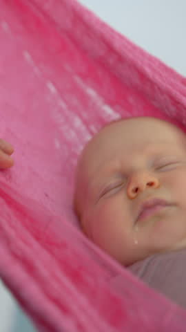 Loving father gently swings his swaddled two-month-old baby in a hammock to help him fall asleep, creating a peaceful and nurturing family bedtime moment.