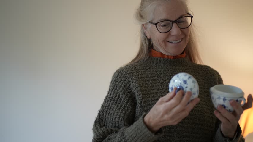 Mature woman smiles as she carefully opens boxes containing family antiques and heirlooms in her living room.