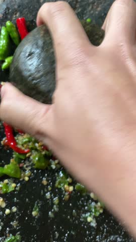 A stone mortar with green and red chilies, ready to be ground, softening the chilies while showcasing traditional Indonesian kitchen tools.