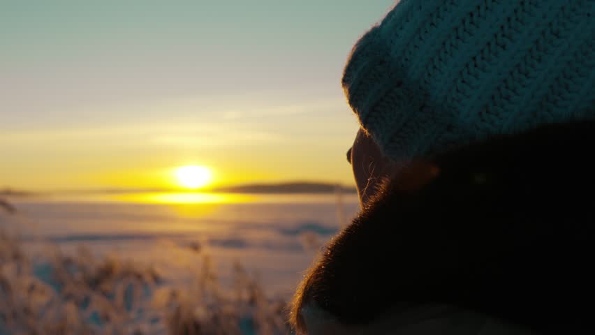 A young girl stands on the shore of a frozen lake and admires the beautiful winter sunset. A frosty winter evening. People in winter.