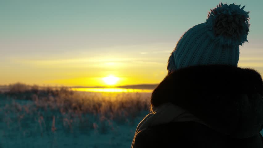 A young girl stands on the shore of a frozen lake and admires the beautiful winter sunset. A frosty winter evening. People in winter.